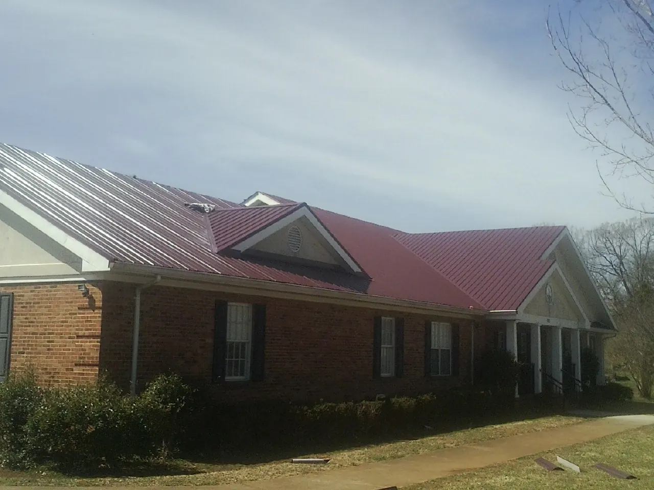 Red metal roof with gabled entries on a long brick building, from a Hail Damage Roof Repair job in Lake Havasu City