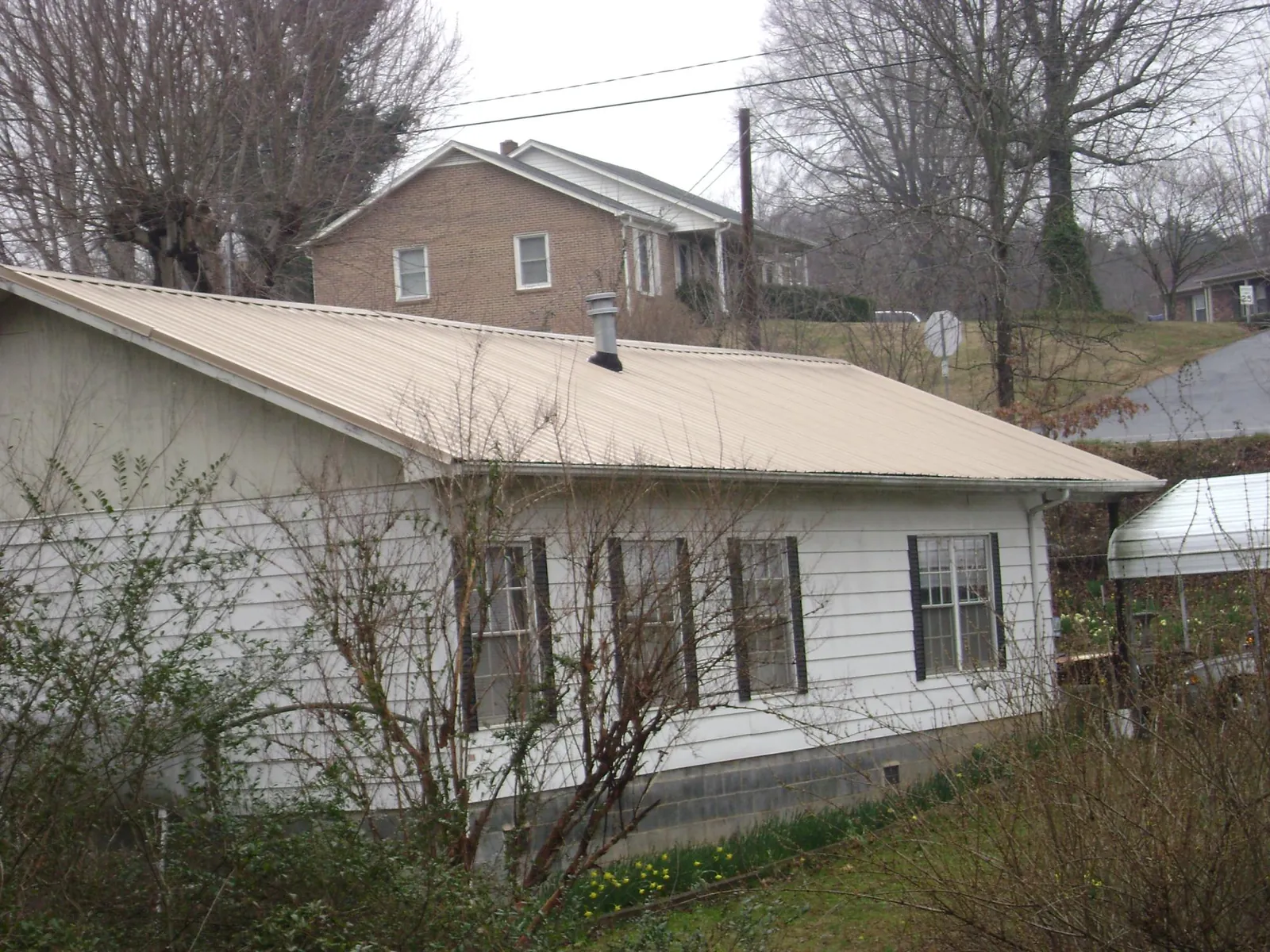 Tan metal roof on a white sided house set into a hillside — Commercial Roofing by Roofing Brothers in Lake Havasu City